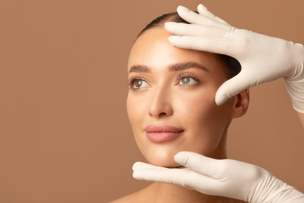 Skin assessment: gloved hands gently framing a client’s face
